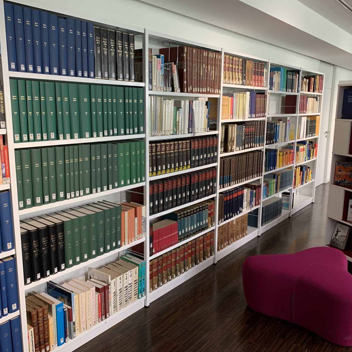 Großes Bücherregal, davor eine gepolsterte Sitzgelegenheit und ein Buchpräsentationsständer