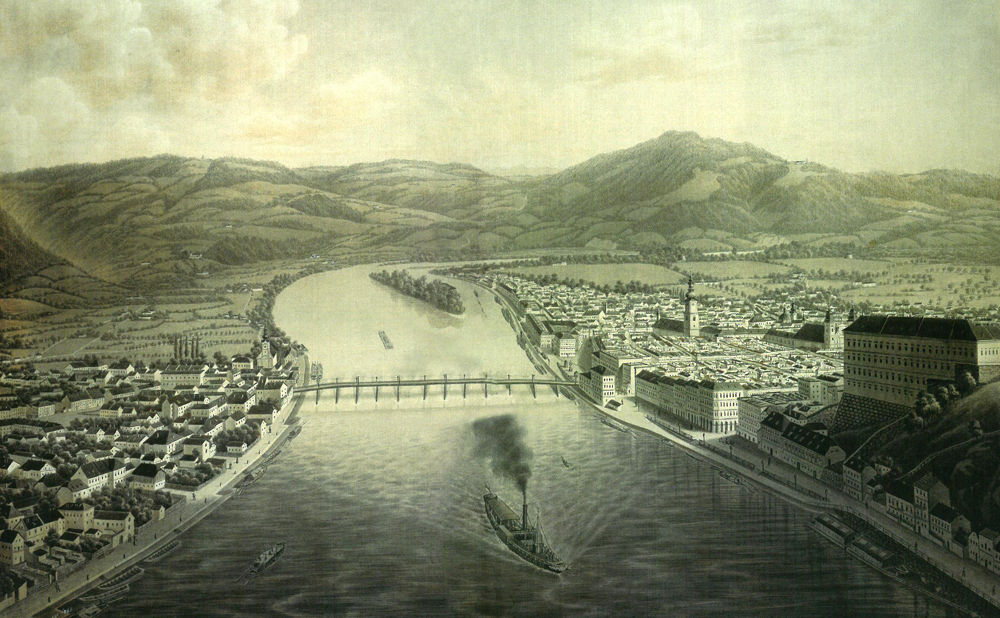 Kolorierter Stich; in der Bildmitte die Donau mit einer Holzbrücke, im Vordergrund ein Raddampfer, im Hintergrund bewaldete Hügel, an den Ufern Häuser, am rechten Ufer das Zentrum von Linz