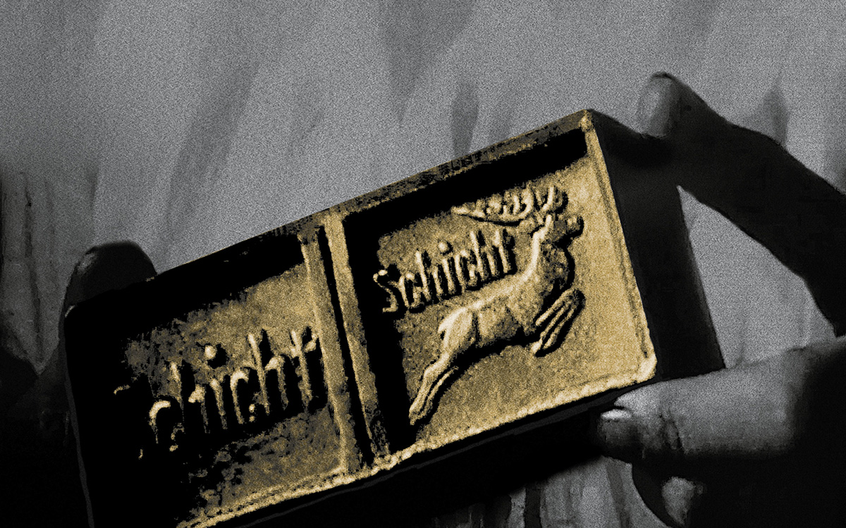 Schwarzweiß-Foto mit gold eingefärbtem Stück Seife, links und rechts jeweils zwischen zwei Fingern gehalten. Auf der Seife ist ein Hirsch und der Schriftzug 
